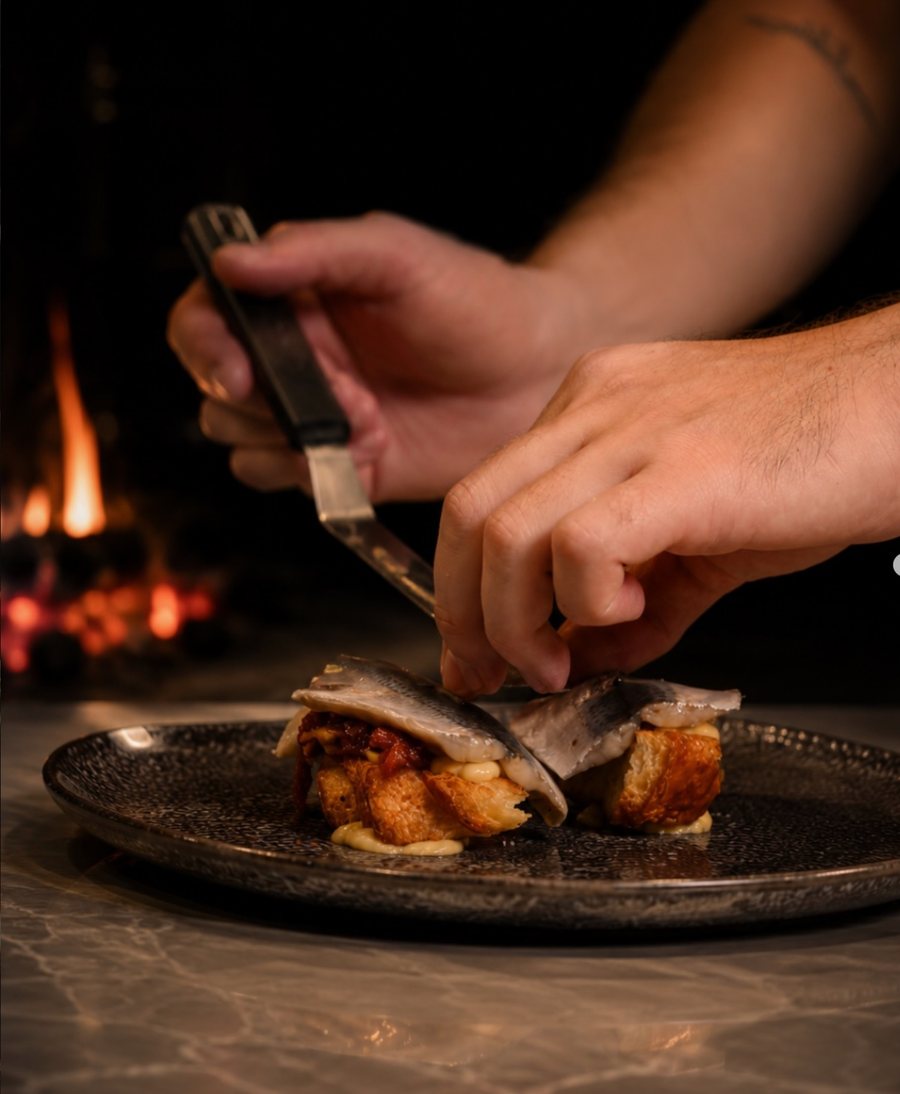 Hands finishing a plated dish beside the fire